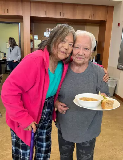 Two women standing together holding a plate of food.